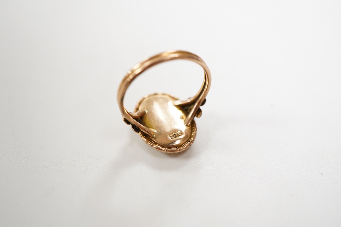 An early 20th century 9ct oval ring, decorated with the figure of a lady in relief, on a butterfly wing ground, beneath a glazed panel, size K, gross weight 2.3 grams.
